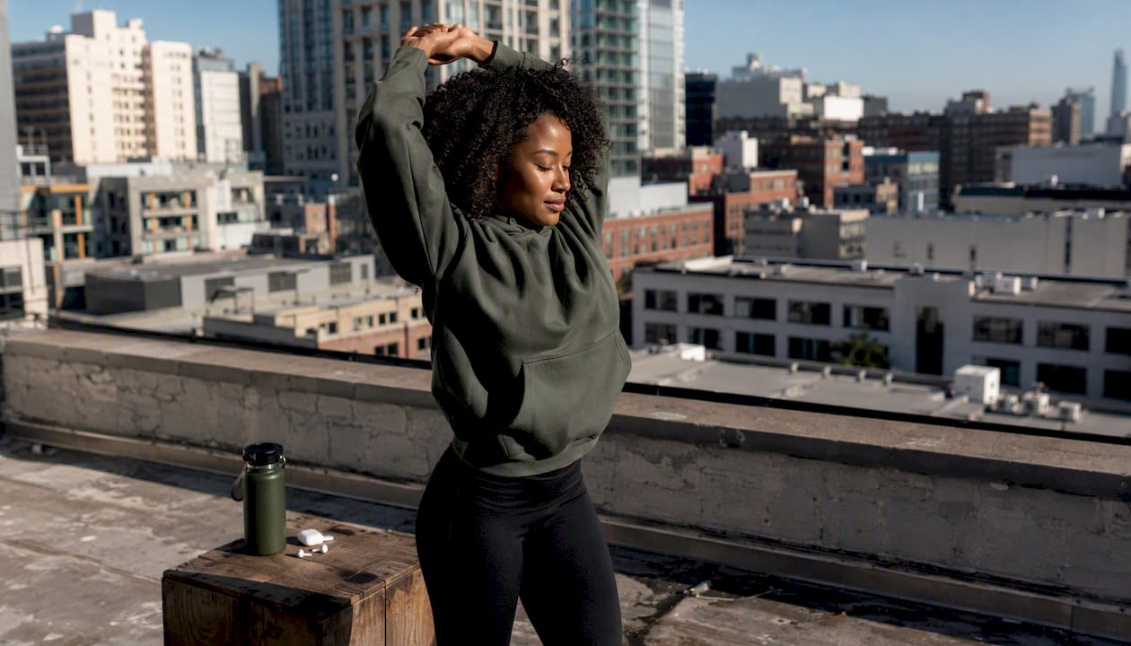 Athlete stretching on urban rooftop in hoodie