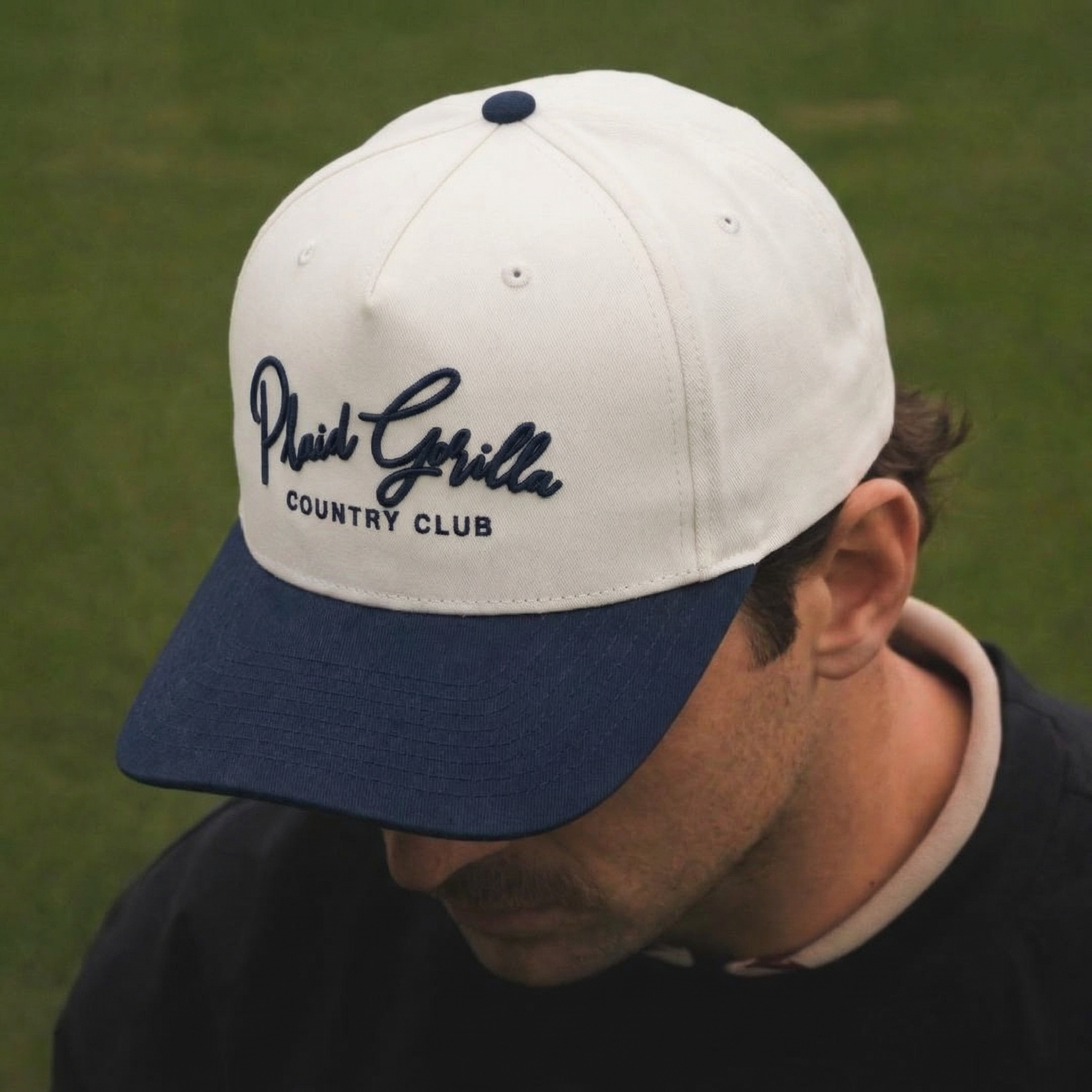 Person wearing a white and navy cap with 'Plaid Gorilla Country Club' text on a green background